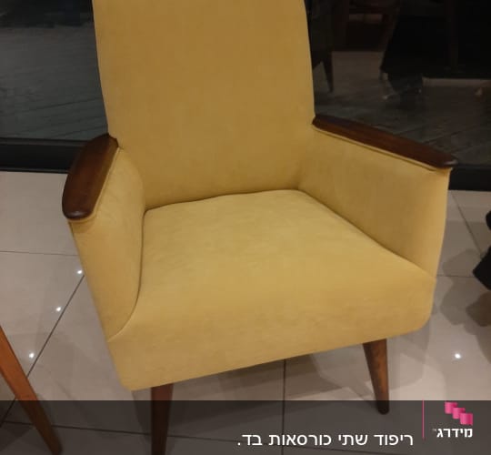 כורסה צהובה עם ריפוד עבה ורגלי עץ כהות